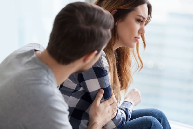 man comforting woman while sitting indoor