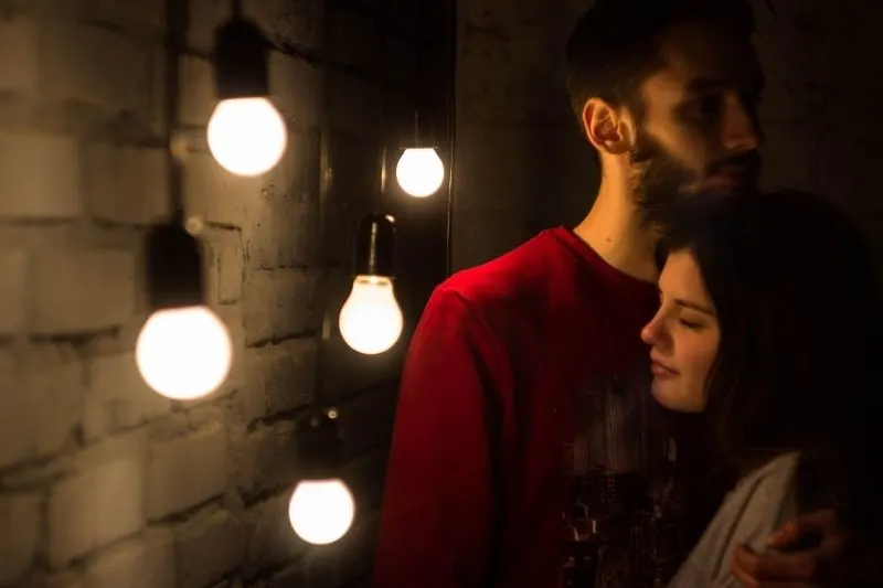 man embracing the woman beside the wall with a series of incandescent bulb