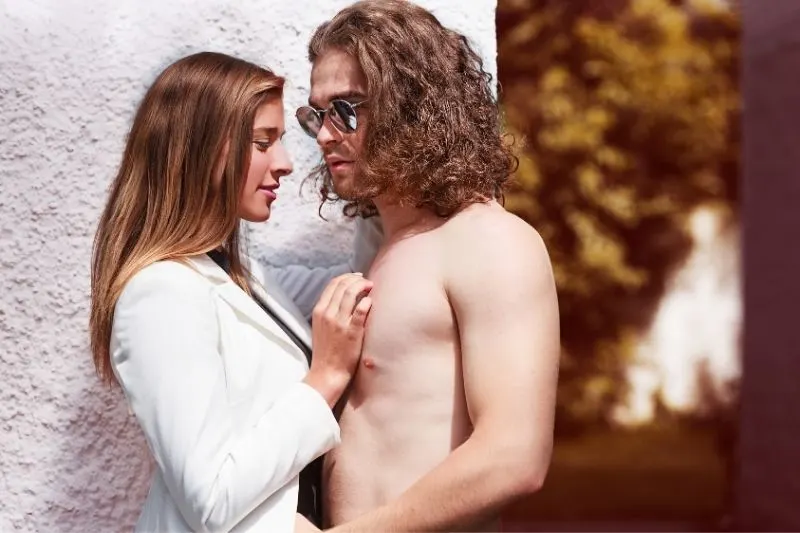 man half naked with long curly hair close to a woman in business wear