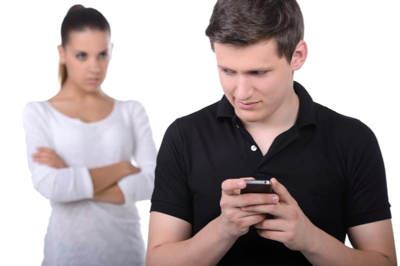 man hiding his smartphone from a jealous woman looking at him