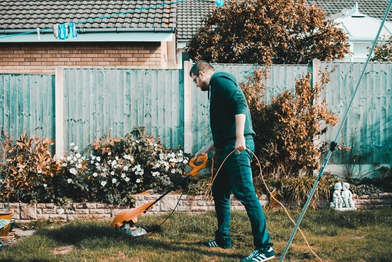 homem segurando um cortador de relva elétrico cor de laranja