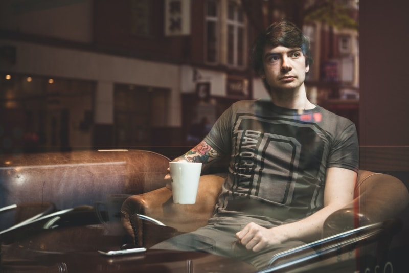 man holding white mug while sitting on armchair