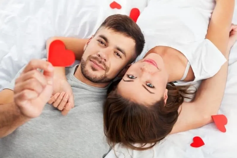man showing paper heart with a woman beside her lying in opposite direction