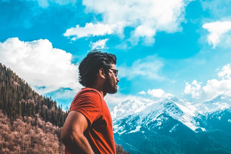 man in orange t-shirt standing near mountain