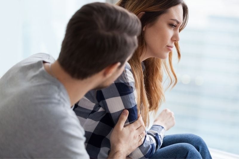 man trying to console an upset woman inside the living room