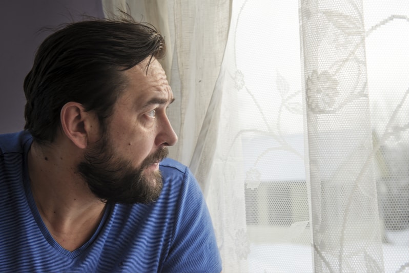 middle-aged man sitting by the window looking outside pensively
