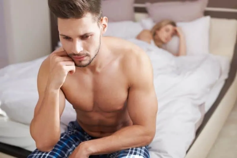 pensive man at bed half naked with a woman sleeping in bed