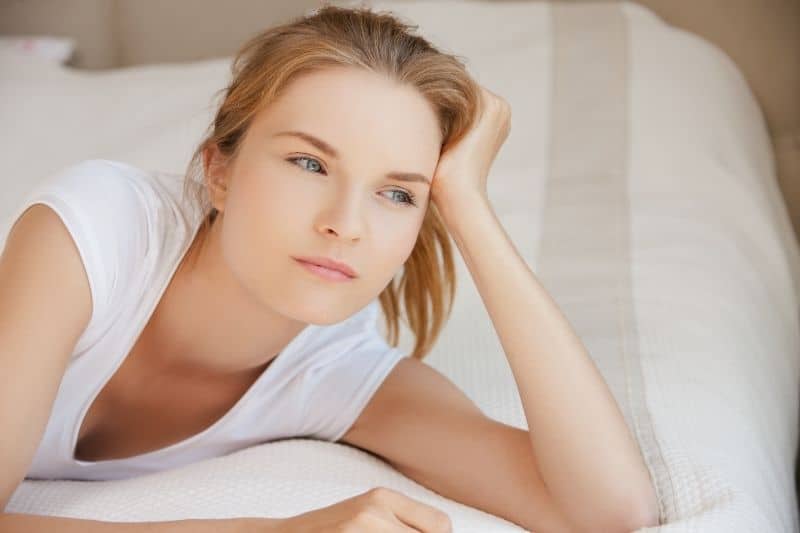 pensive teenage girl lying on bed with hand supporting head