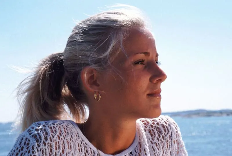 pensive woman near the body of water wearing a white knitted top