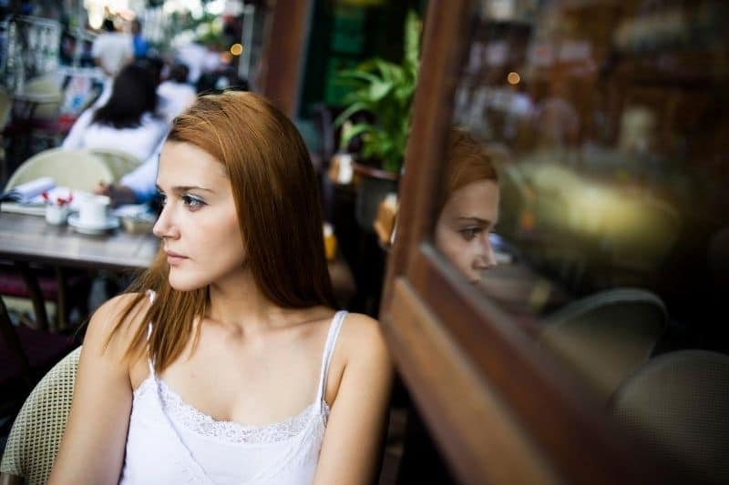 donna pensierosa seduta da sola in un caffè all'aperto che guarda il lontano