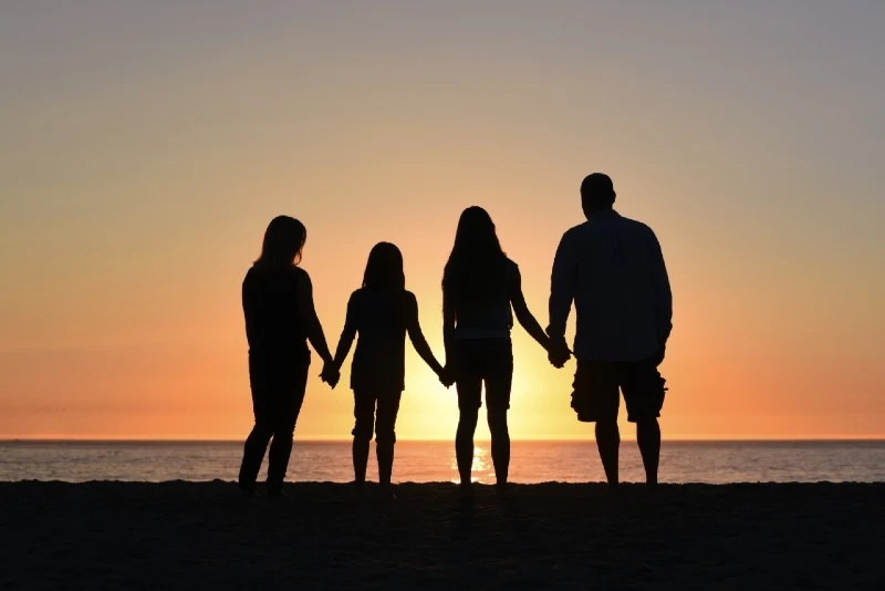 four people holding hands while looking at sea