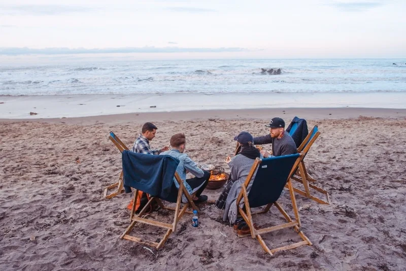 group of people sitting on beach near fire pit