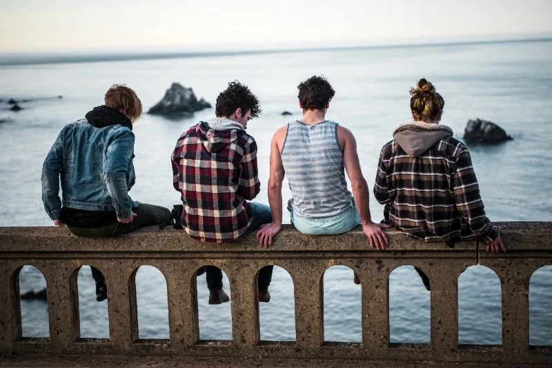 four people sitting on bench looking at sea