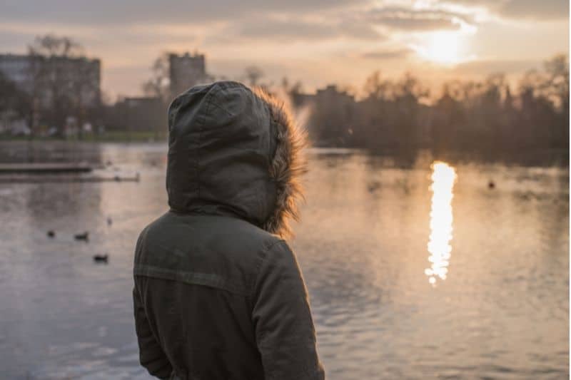 person wearing hoodie facing a body of water during sunset/sunrise