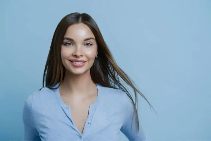 portrait of a woman wearing blue top standing against a blue wall