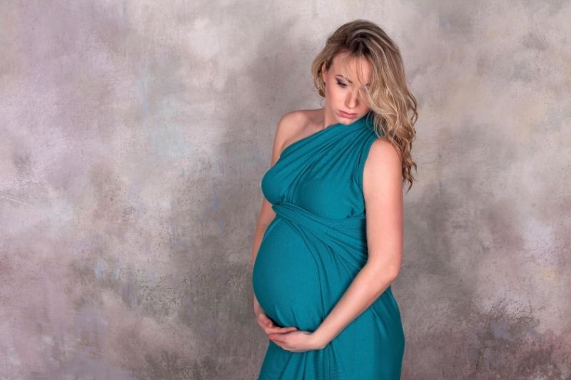 pregnant woman in blue dress posing against a gray wall 