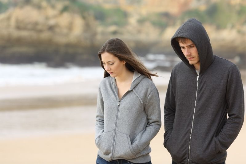 coppia triste che cammina sulla spiaggia indossando maglioni