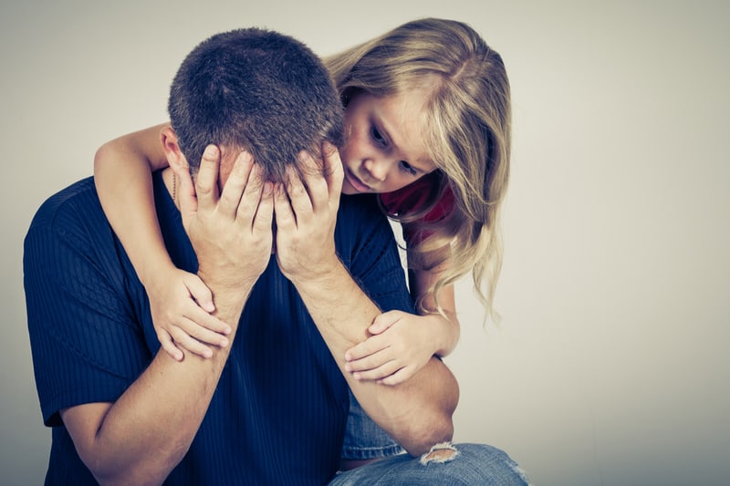 sad father comforted by his daughter hugging him