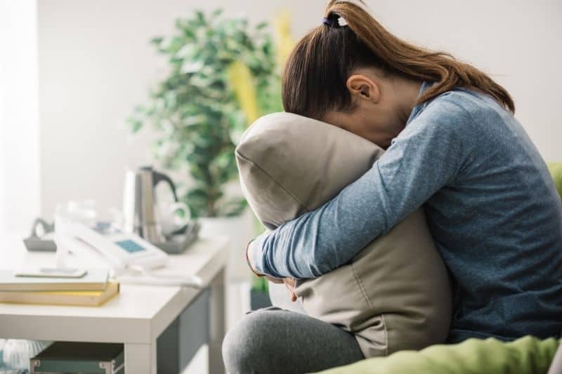 sad woman hugging a pillow sitting on the couch in sideview
