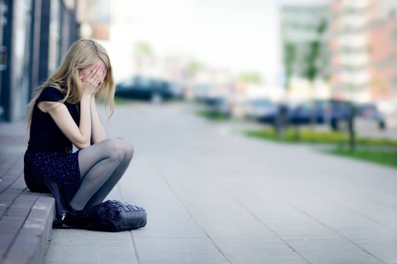 joven triste llorando tapandose la cara sentada al borde de la carretera