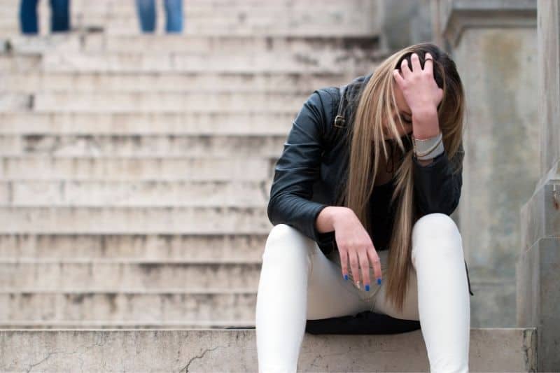 una joven triste sentada en las escaleras del campus 