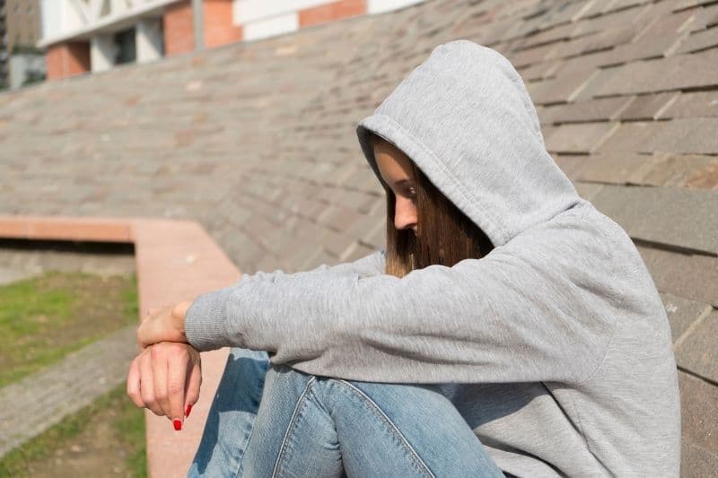 joven triste con capucha sentada al aire libre