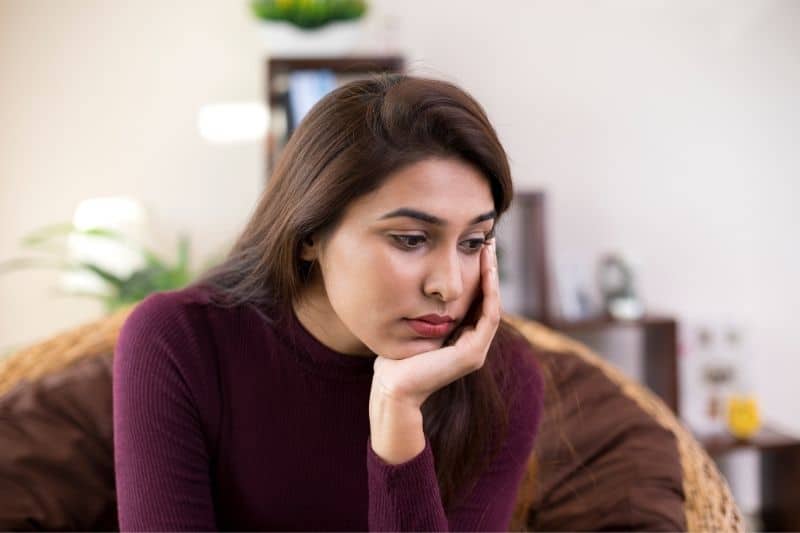 mulher jovem e triste sentada num sofá castanho numa sala de estar