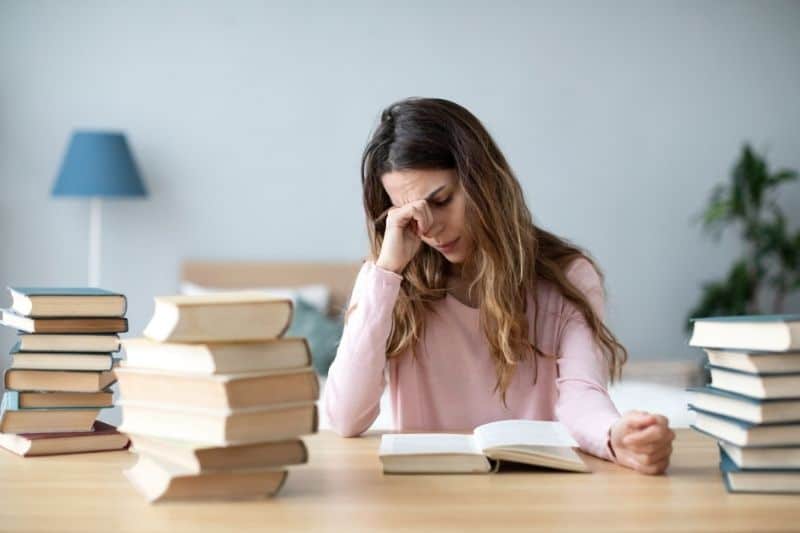 mulher jovem triste com livros em cima da secretária a ler