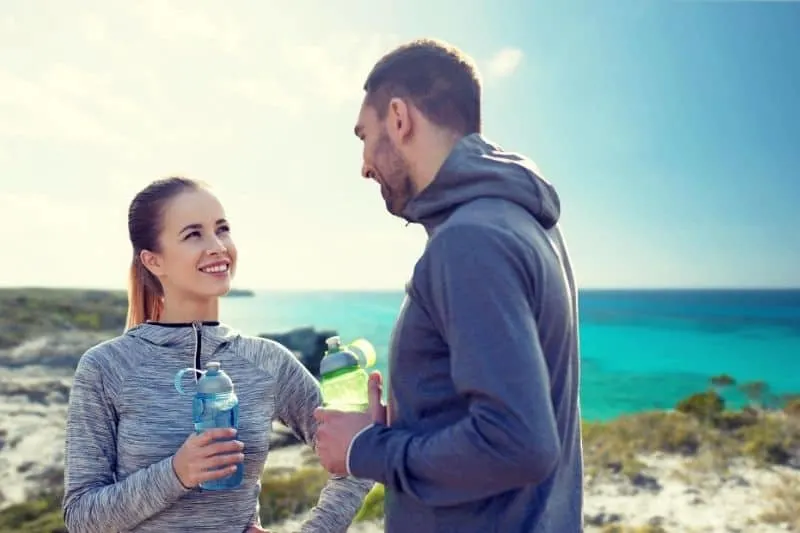 smiling couple drinking water from the drinker wearing athletic wear near the sea