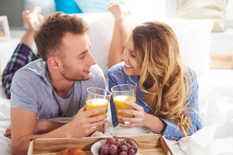 smiling couple eating healthy breakfast at bed