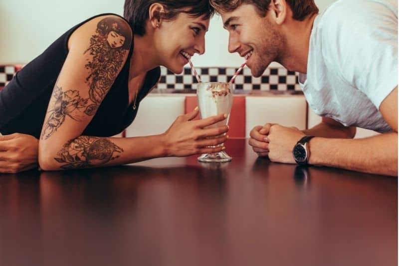 tattoed woman and non tattoed man enjoying one milkshake together 