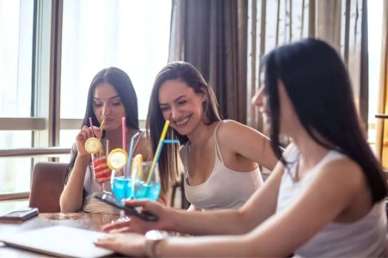 three women friends enjoying cocktail at home wearing white tank top