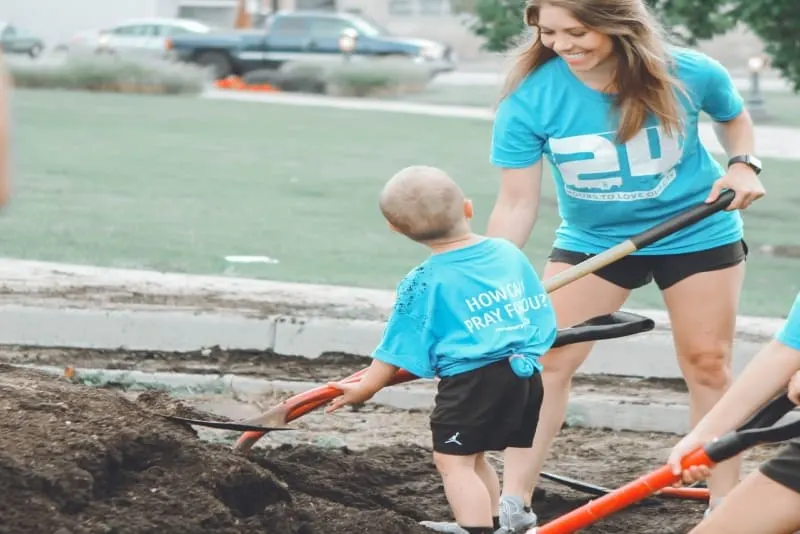 toddler holding brown and black shovel while standing near woman