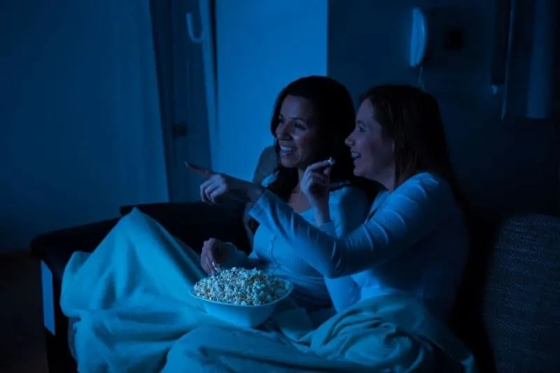 two women chilling watching tv in the home's couch in the night 