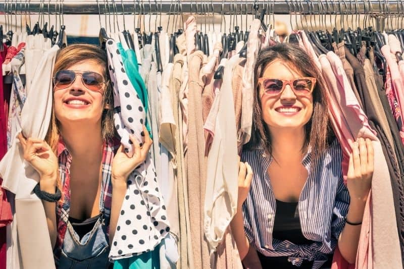 two women having fun in between hanged clothes in the wardrobe