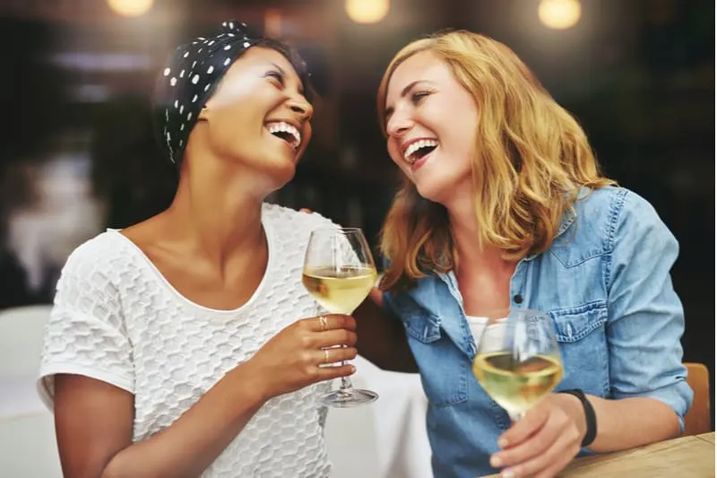 two women laughing hard while drinking wine in a bar