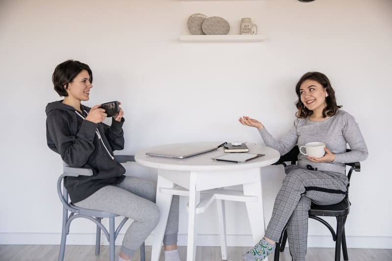 two women talking to each other in athletic wear over a cup of coffee