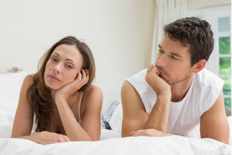 upset woman talking with a man lying down on their bed with white linen