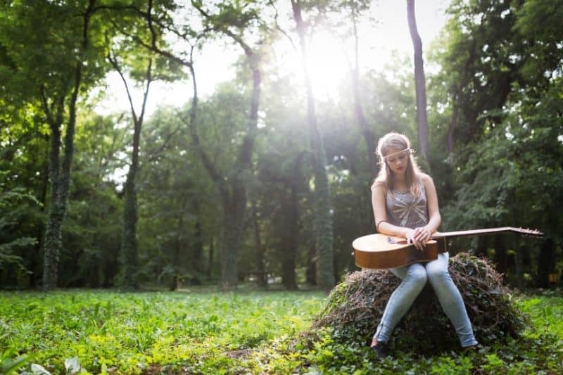vista di una donna con il cuore spezzato seduta su una roccia all'aperto con una chitarra in grembo