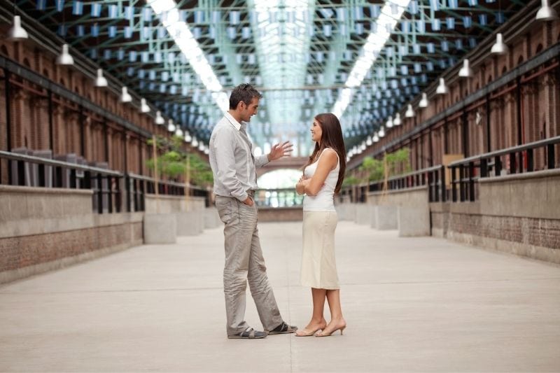 mujer y hombre de pie en pasillo cubierto mientras hablan