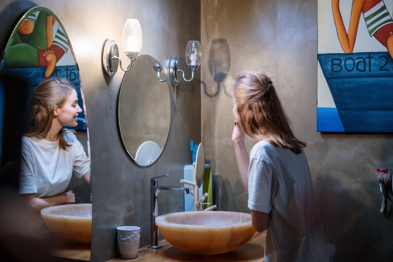 donna che si lava i denti in piedi vicino allo specchio