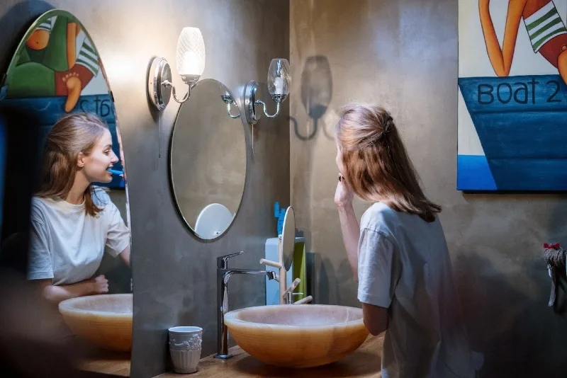 woman brushing teeth while standing near mirror