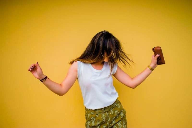 mujer con top blanco bailando cerca de una pared amarilla