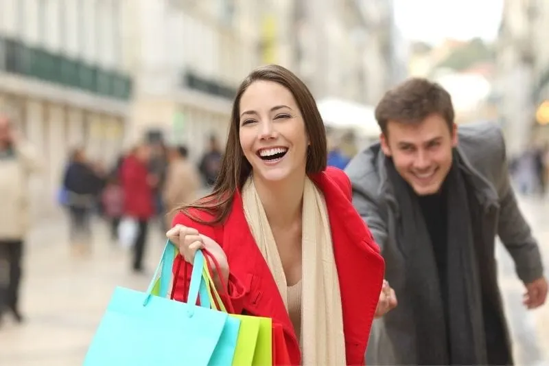 woman dragging the man on shopping while carrying shopping bags