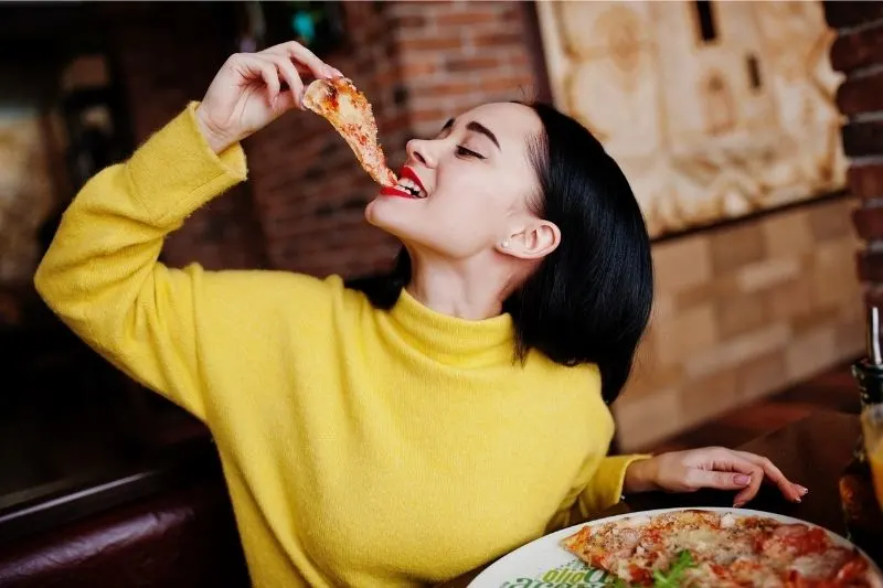 woman eating pizza inside a pizza house cheerfully