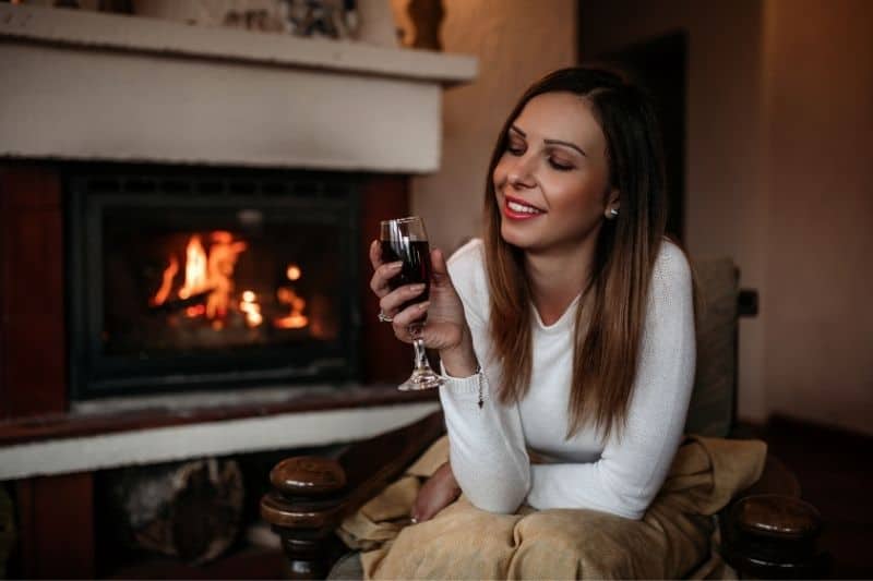 donna che gode da sola in casa con il vino vicino al camino