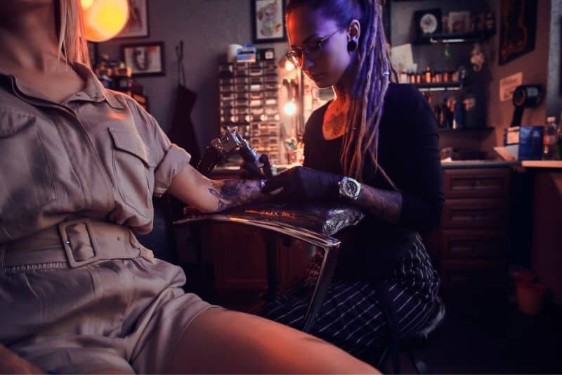 donna che si fa un tatuaggio con una donna che mette l'inchiostro sul braccio di un'altra donna