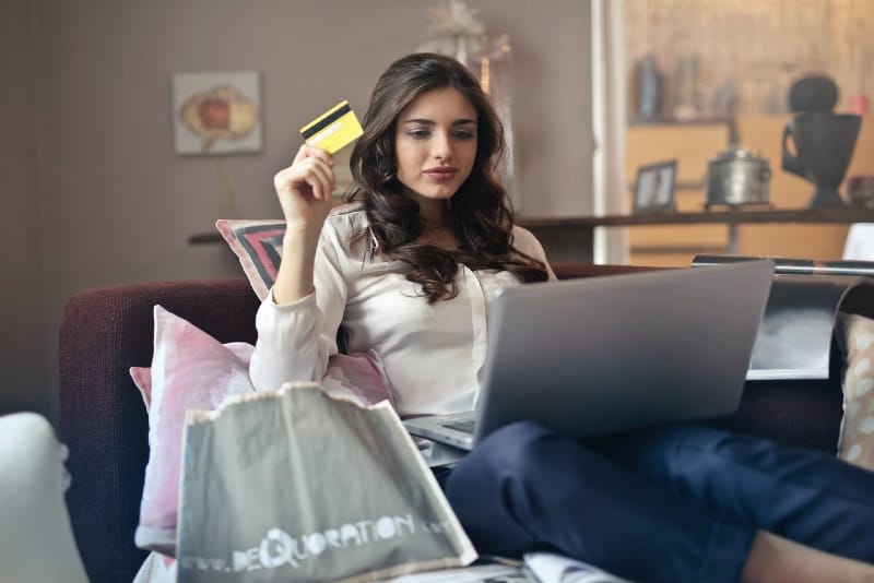 mujer sosteniendo una tarjeta de crédito mientras mira un portátil