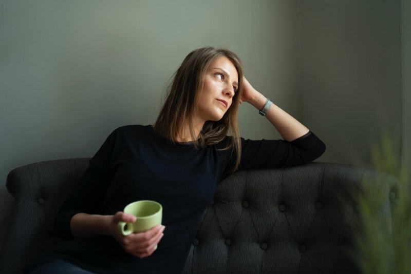 mulher a segurar uma caneca verde enquanto está sentada no sofá