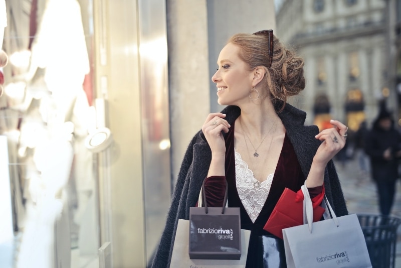 mulher de blazer preto segurando sacos de compras